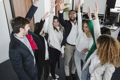 Glückliche Geschäftskollegen mit erhobenen Armen im Coworking-Büro - EBBF05441