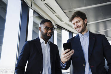 Glückliche Geschäftsleute teilen sich ein Smartphone in einem Coworking-Büro - EBBF05452