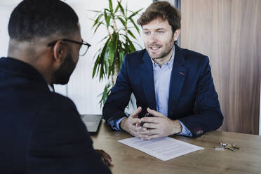 Geschäftsmann im Gespräch mit einem Kollegen am Schreibtisch in einem Coworking-Büro - EBBF05457