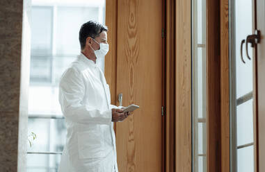 Wissenschaftler mit Gesichtsschutzmaske und Tablet-PC in einer medizinischen Klinik - JOSEF06933