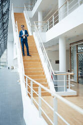 Businessman standing on steps in office - JOSEF06945