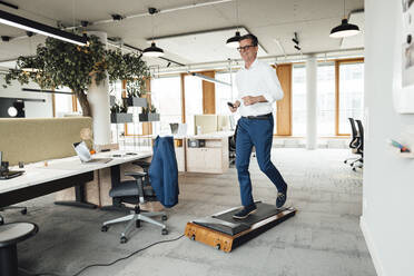 Smiling businessman running on treadmill at office - JOSEF06951