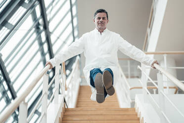 Playful scientist balancing on steps railing at medical clinic - JOSEF06966