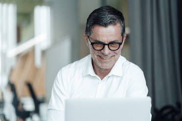 Smiling businessman with eyeglasses working at office - JOSEF06978