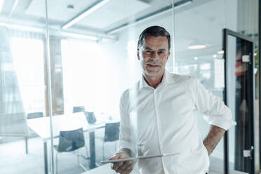 Working man with tablet PC leaning on glass wall at office - JOSEF06987