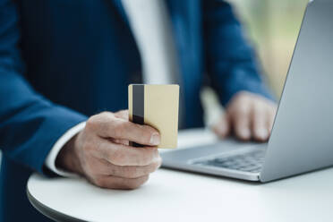 Hand of businessman holding credit card using laptop on table at office - JOSEF06996