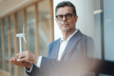 Businessman holding wind turbine at office - JOSEF06999
