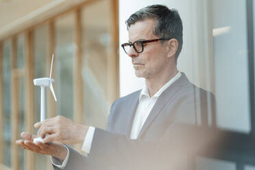 Businessman with eyeglasses looking at wind turbine at office - JOSEF07000