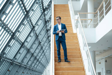 Working man standing on staircase holding tablet PC at office - JOSEF07003