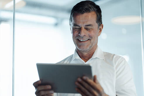 Lächelnder Geschäftsmann mit Tablet-PC im Büro - JOSEF07016