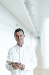 Smiling scientist with tablet PC standing at medical clinic - JOSEF07027