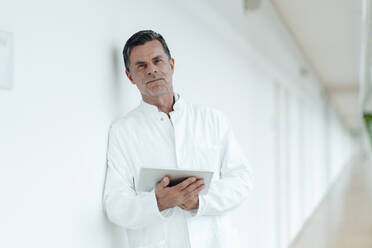 Scientist with tablet PC leaning on wall at medical clinic - JOSEF07029