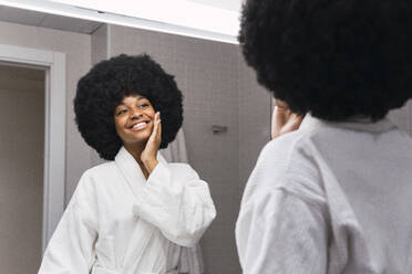 Glückliche Frau bei der Hautpflege im Spiegel im Badezimmer - PNAF02998