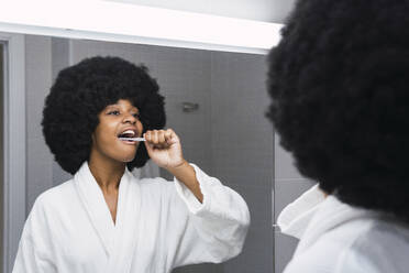 Afro-Frau beim Zähneputzen und Blick in den Spiegel zu Hause - PNAF03001