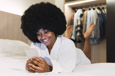 Smiling woman using smart phone on bed at home - PNAF03017