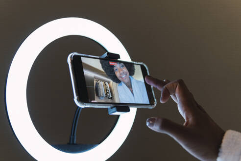 Smiling woman vlogging on smart phone in illuminated ring light - PNAF03021