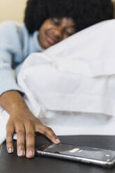 Frau schaltet den Alarm auf ihrem Smartphone im Schlafzimmer zu Hause aus - PNAF03033
