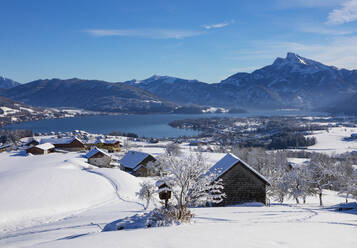 Austria, Upper Austria, Mondsee, Snowy landscape of Salzkammergut with huts in foreground and Mondsee lake in background - WWF06068