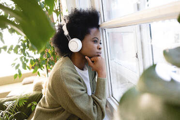 Thoughtful woman listening music through headphones at home - VPIF05250