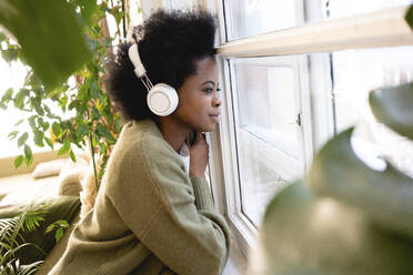 Junge Frau hört Musik und schaut durch das Fenster zu Hause - VPIF05251