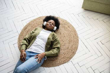 Junge Frau entspannt sich und hört Musik über Kopfhörer auf dem Boden liegend - VPIF05254