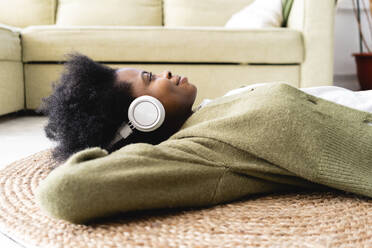 Nachdenkliche Frau, die zu Hause über Kopfhörer Musik hört - VPIF05255