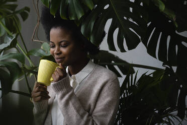 Junge Frau riecht Kaffee bei Grünpflanzen - VPIF05265