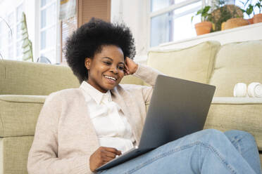 Happy freelancer using laptop by sofa in living room at home - VPIF05267