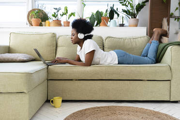 Young businesswoman with headphones using laptop on sofa at home - VPIF05299