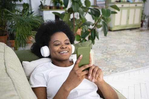 Glückliche Frau benutzt ihr Smartphone und hört Musik auf dem Sofa im Wohnzimmer - VPIF05305
