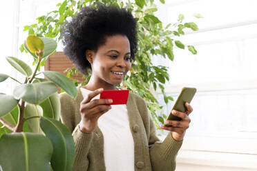 Lächelnde Frau mit Kreditkarte beim Online-Shopping auf dem Smartphone zu Hause - VPIF05325