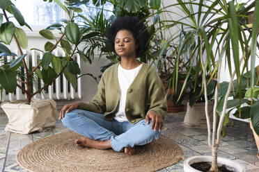 Afro woman meditating amidst plants at home - VPIF05326