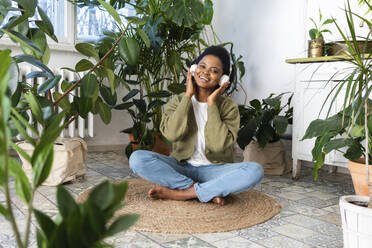 Smiling woman listening music through headphones on rug at home - VPIF05327