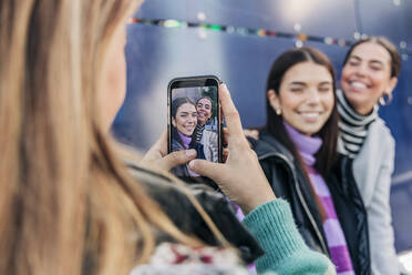 Junge Frau fotografiert Freunde mit ihrem Smartphone - JRVF02687