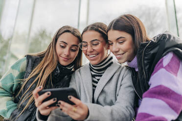 Lächelnde junge Freunde schauen auf ihr Smartphone - JRVF02699