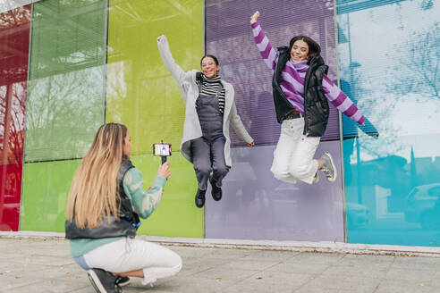 Frau filmt fröhlich springende Freunde mit dem Handy in der Stadt - JRVF02702