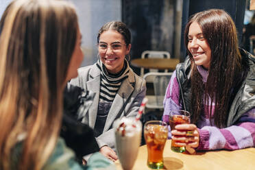 Lächelnde Frauen im Gespräch mit einem jungen Freund in einem Cafe - JRVF02713