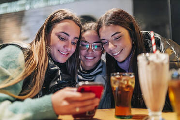 Lächelnde junge Frauen teilen sich ein Smartphone in einem Cafe - JRVF02714