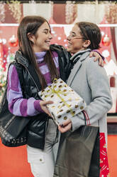 Glückliche Freunde umarmen sich und halten ein Weihnachtsgeschenk in der Hand - JRVF02717