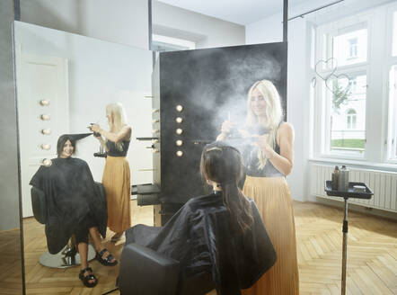 Friseurin sprüht Haarspray auf das Haar einer Frau im Friseursalon - CVF01890