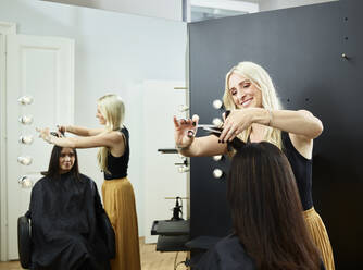 Smiling hairdresser cutting customer's hair in salon - CVF01891