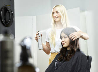 Lächelnde Friseurin, die das Haar einer Frau mit Haarspray im Salon stylt - CVF01894