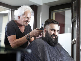 Lächelnder Friseur, der einem Mann im Friseursalon die Haare schneidet - CVF01898