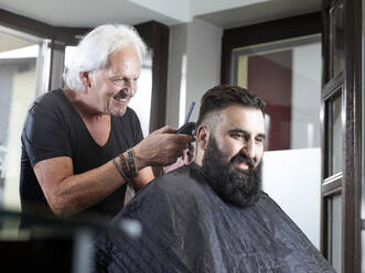Smiling hairdresser cutting man's hair in hair salon - CVF01898