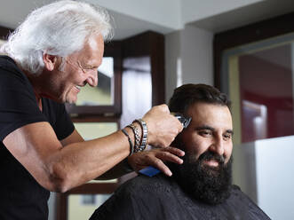 Lächelnder Friseur, der einem Mann die Haare mit einem elektrischen Rasiermesser schneidet - CVF01899