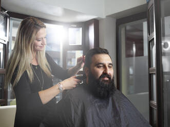 Friseurin schneidet einem Mann die Haare mit einem elektrischen Rasiermesser im Salon - CVF01901