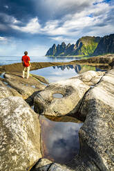 Wanderer, der die scharfen Felsen der Bergspitzen betrachtet, die neben Felsbecken stehen, Tungeneset, Senja, Provinz Troms, Norwegen, Skandinavien, Europa - RHPLF21405