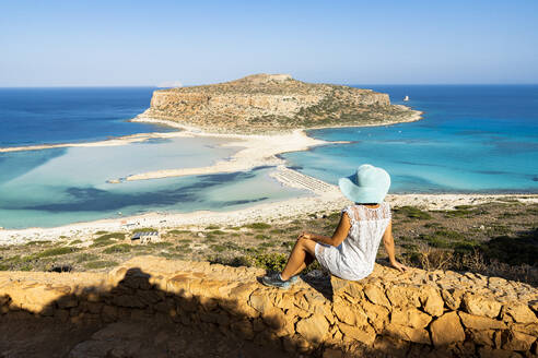 Charmante Frau mit Sonnenkleid und Hut, die das kristallklare türkisfarbene Meer und die Lagune betrachtet, Balos, Kreta, Griechische Inseln, Griechenland, Europa - RHPLF21408