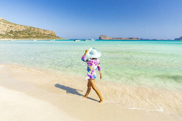 Beautiful woman with sun hat walking on idyllic empty beach, Crete, Greek Islands, Greece, Europe - RHPLF21410