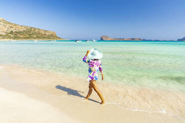 Schöne Frau mit Sonnenhut spaziert am idyllischen leeren Strand, Kreta, Griechische Inseln, Griechenland, Europa - RHPLF21410